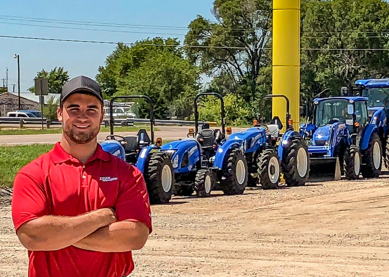 Business of Sales Intern in front of New Holland tractors